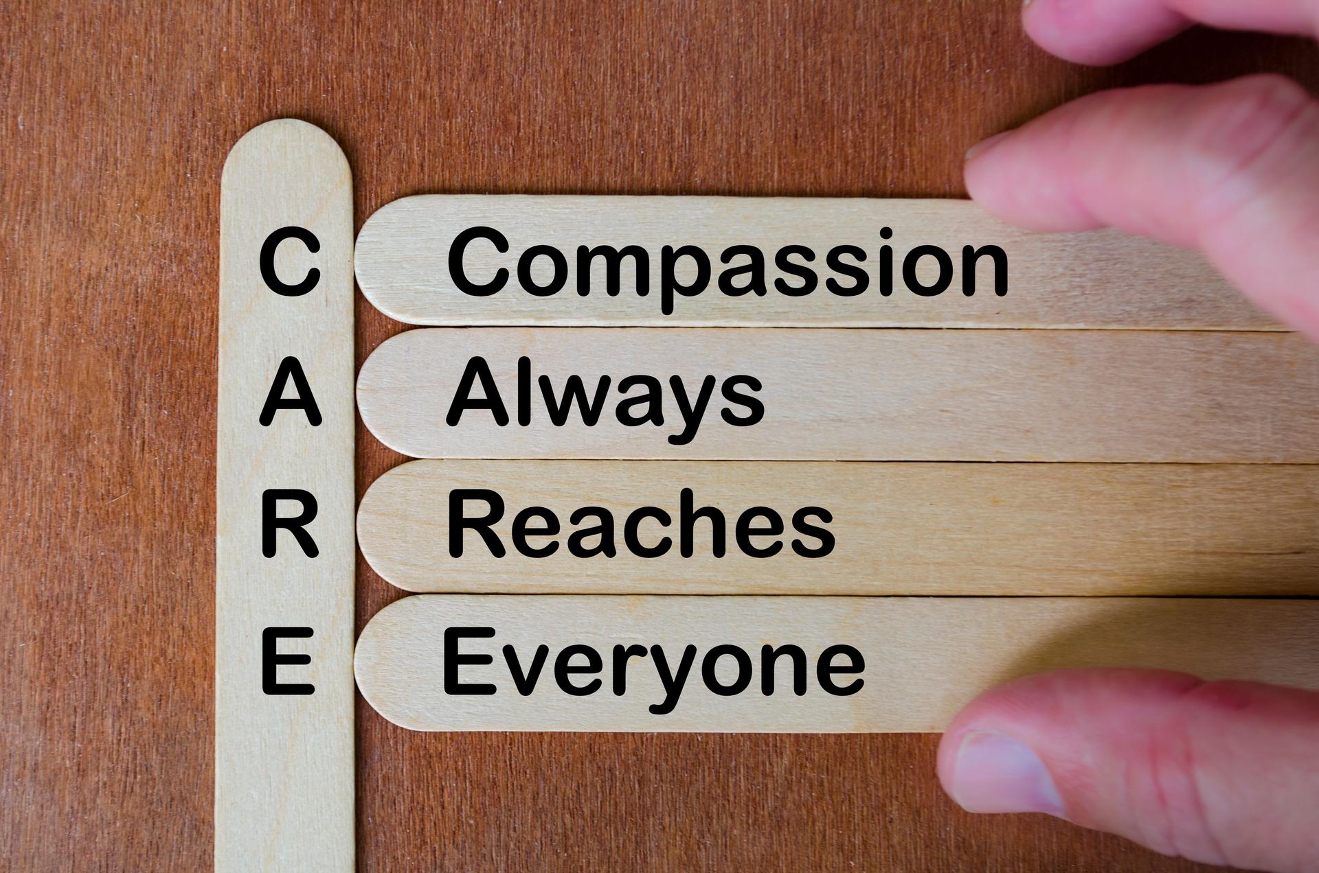 Wooden stick acronym CARE emphasizing compassion, empathy, inclusion, diversity, kindness, and humanity in teamwork values