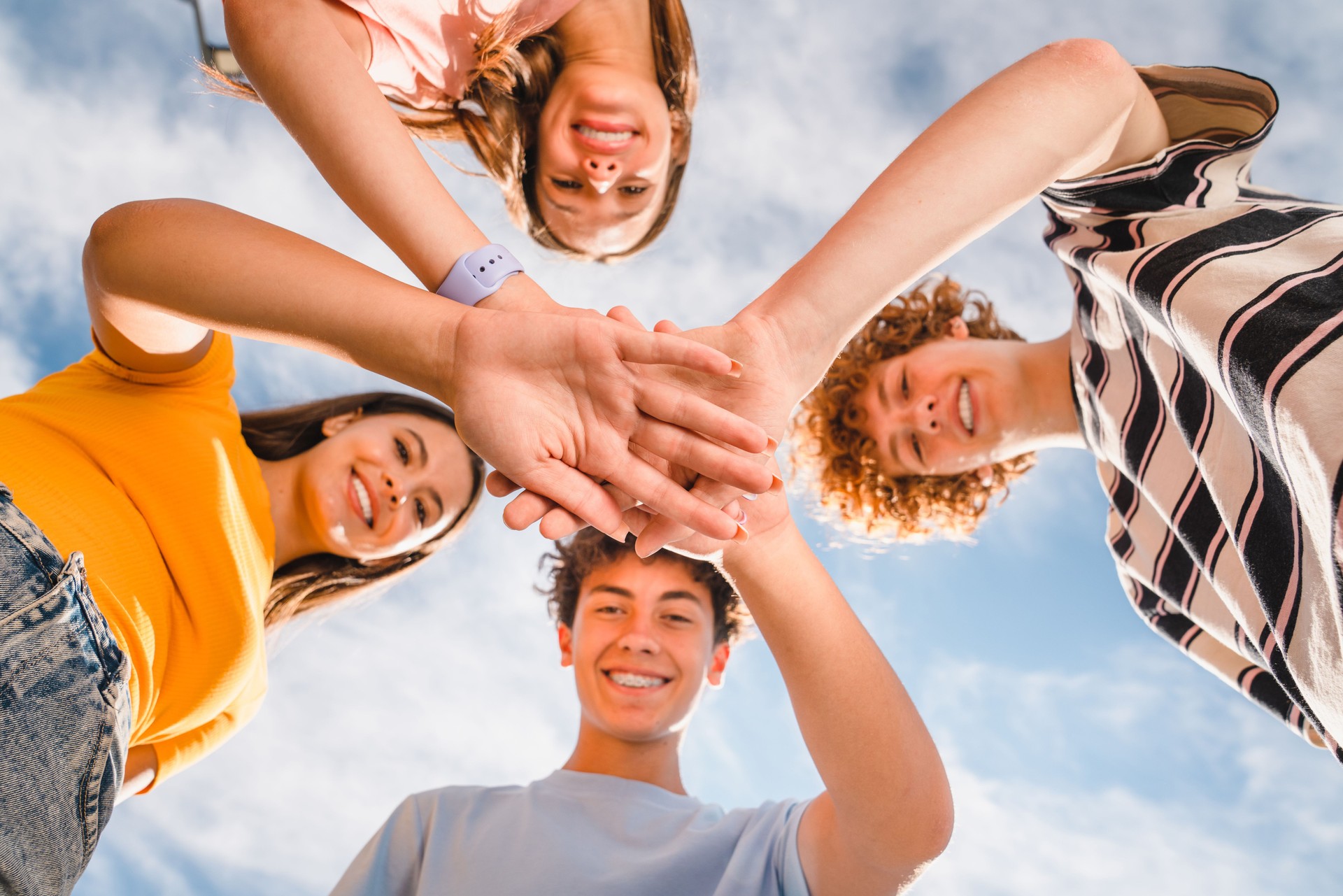 Low angle view of smiling boys and girls in casual giving high five stacking hands together outside